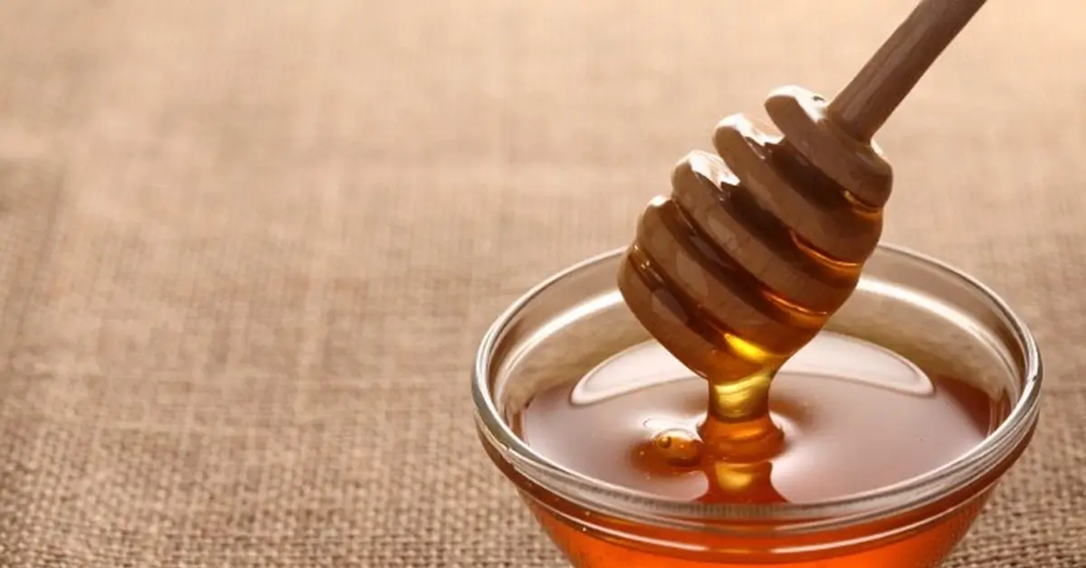 Honey being drizzled onto a wooden spoon.