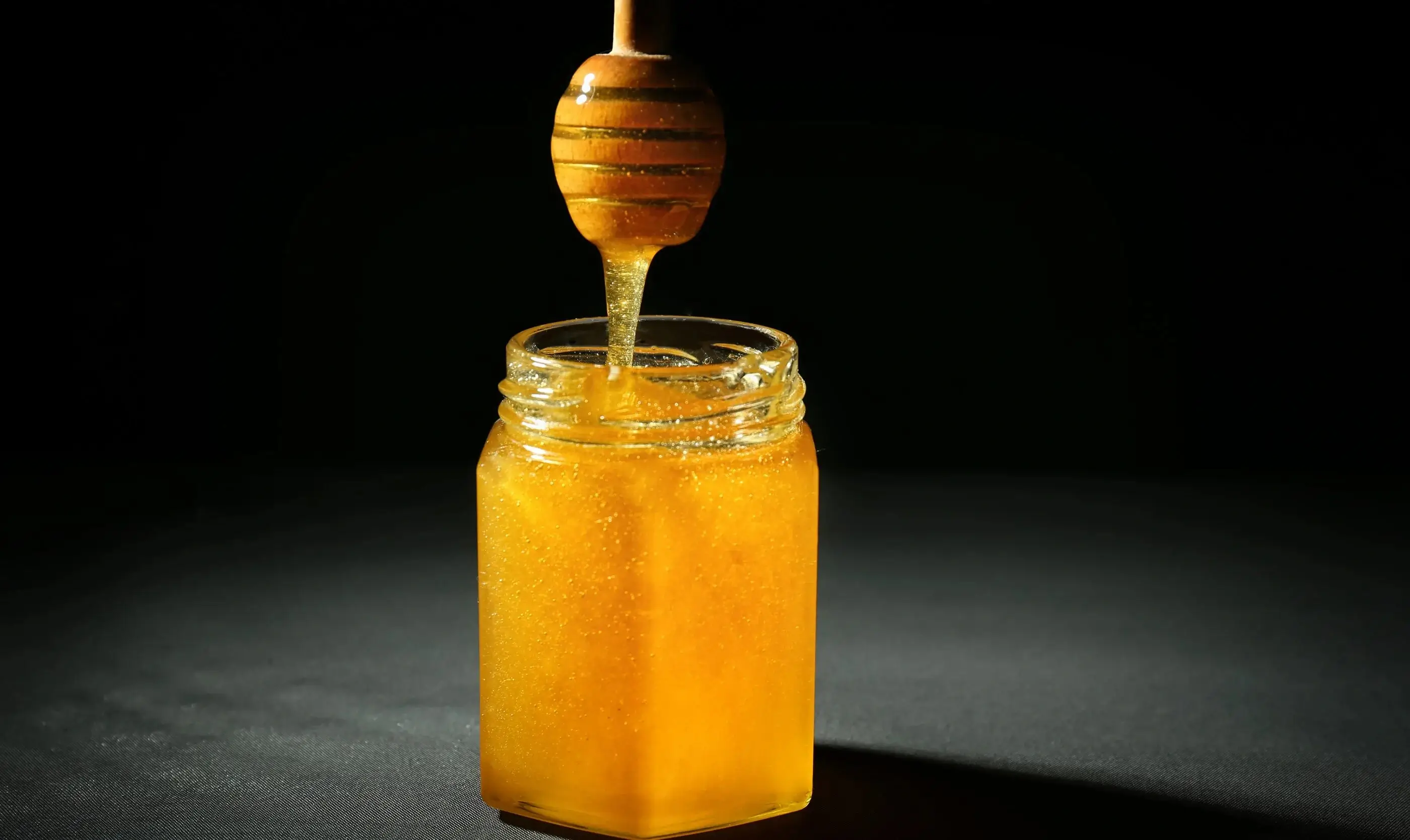 A jar of golden honey against a dark background.